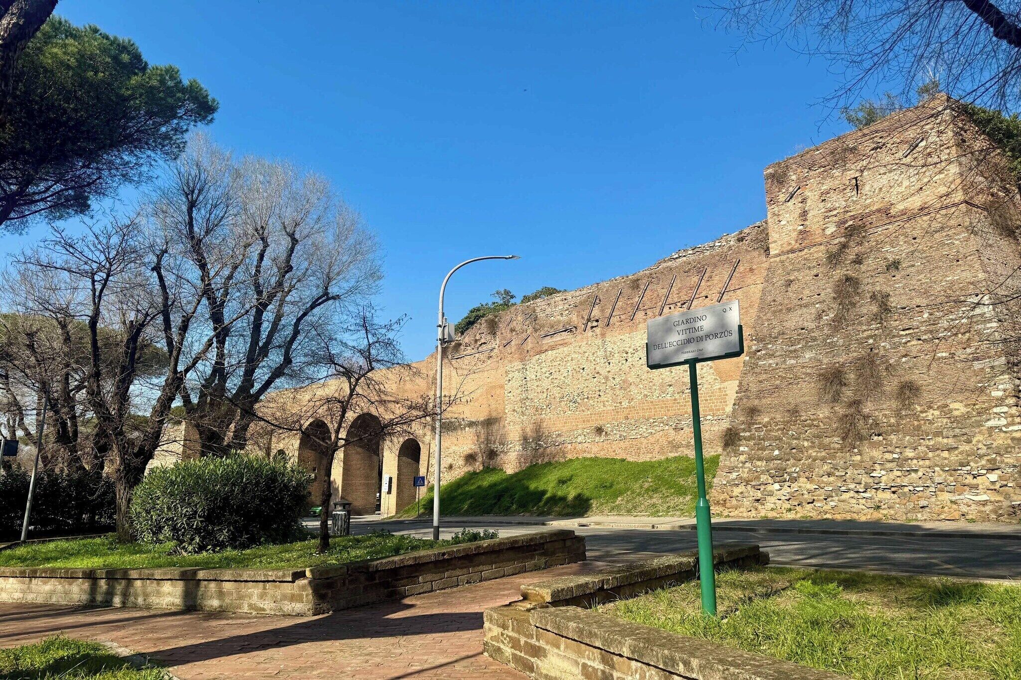 Un mur de pierre ancien, doté d’une entrée en arc de cercle, un panneau de signalisation et un lampadaire.