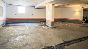 An indoor parking garage with concrete floors and walls, marked parking spaces, and two illuminated wall-mounted lights.