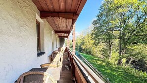 Un'area salotto esterna coperta con mobili in vimini, ringhiera in legno e vista su un paesaggio verde.