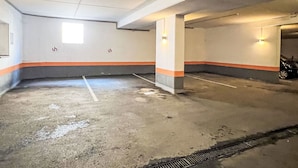 Un parcheggio coperto con pavimenti e pareti in cemento, posti auto delimitati e due luci a parete illuminate.