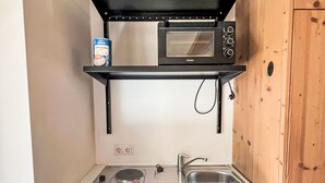 Un angolo cottura compatto con forno a microonde, un piccolo ripiano con una scatola di conserve, un lavello e un piano cottura.