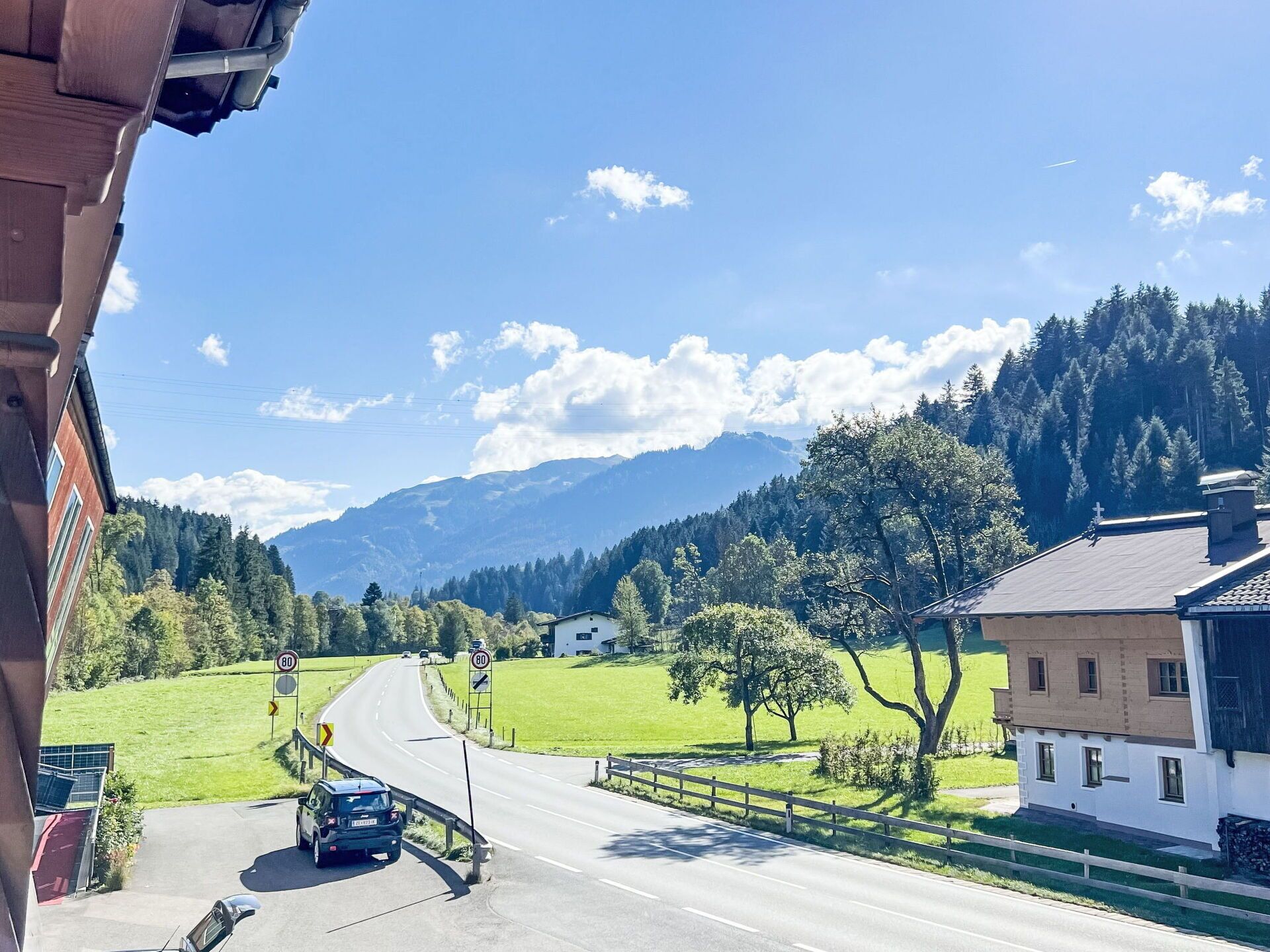 A road with a speed limit sign of 80 km/h, a car, and a building with a sloped roof.