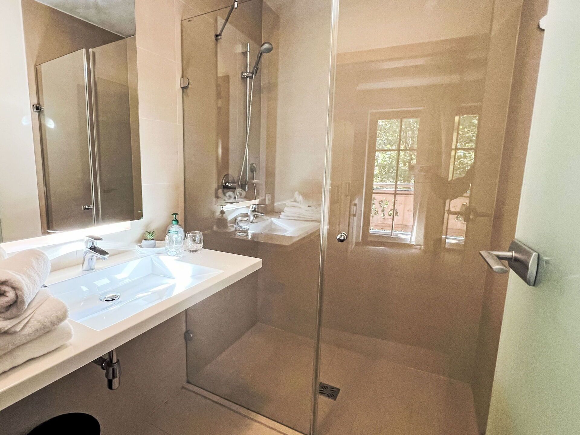 Une salle de bain moderne avec une douche à parois de verre, un grand miroir et un meuble-lavabo avec un évier et un porte-serviettes.