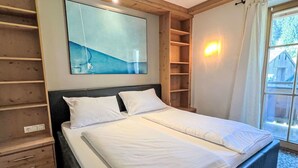 Un dormitorio con cama, cabecera de madera, estante en la pared y ventana con cortinas.