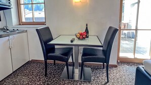 Une petite cuisine équipée d’un four à micro-ondes, d’une table avec des chaises, d’un panier de fruits et d’une bouteille.