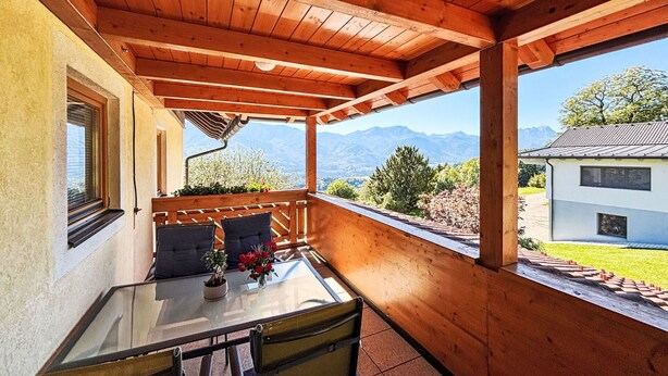 A wooden deck with a glass table and chairs, overlooking a mountainous landscape. - Nice apartment for 4 guests with WIFI, TV and balcony (Ludmannsdorf)