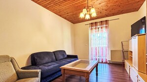 A living room with a wooden ceiling, a sofa, a chair, a coffee table, and a radiator. - Nice apartment for 4 guests with WIFI, TV and balcony (Ludmannsdorf)