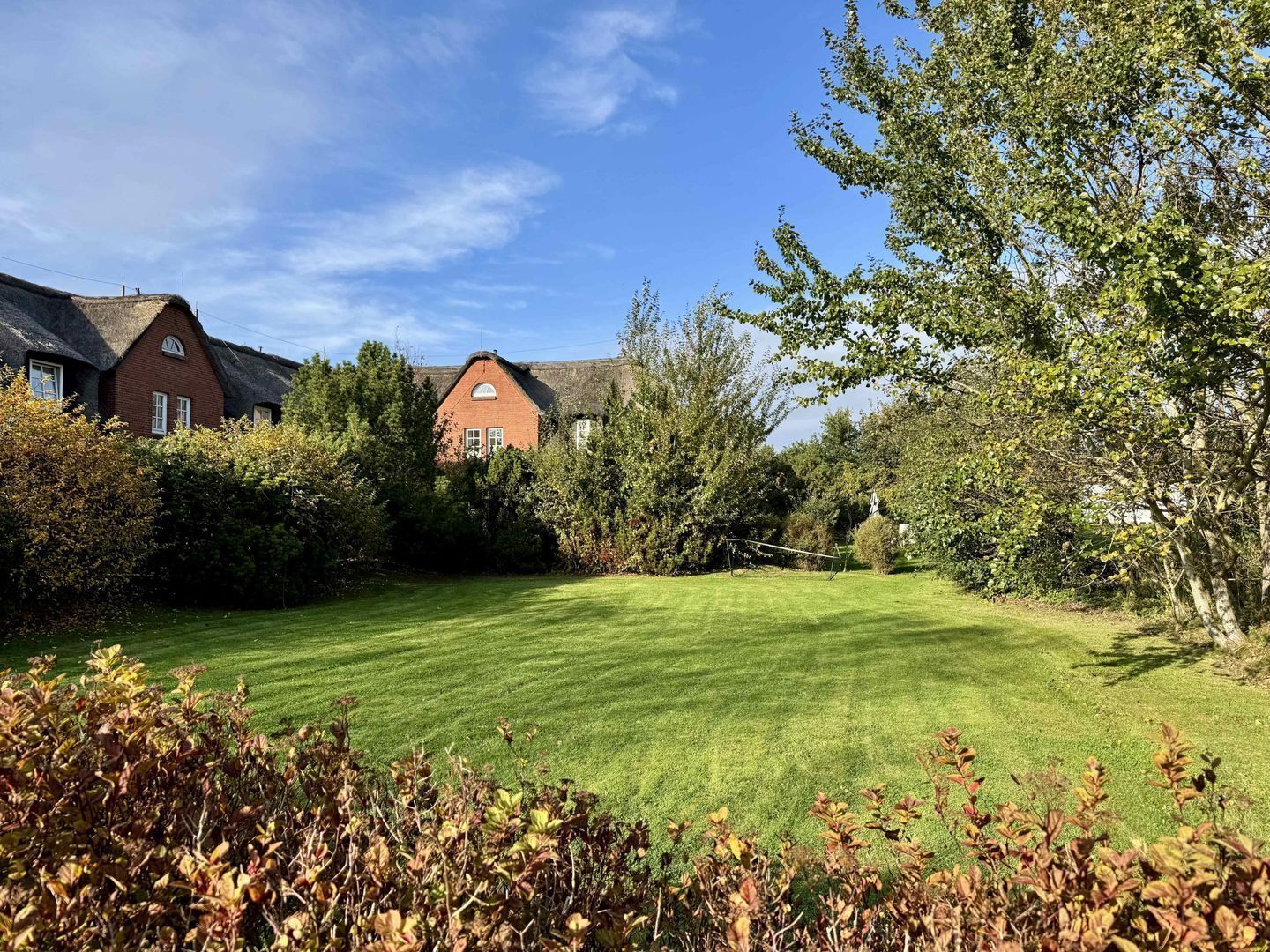 A well-maintained lawn with a thatched-roof building and a red brick house in the background.
