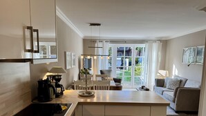 A modern kitchen with a central island, a dining area with a table and chairs, and a living area with a sofa and a TV. - Gaathüs - Stylish vacation home under thatch in Keitum (Sylt-Ost)