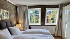 A bedroom with a large bed, two bedside tables, a window with a view of greenery, and a radiator. - Gaathüs - Stylish vacation home under thatch in Keitum (Sylt-Ost)