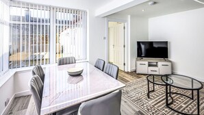 Un espace repas moderne avec une table en verre, des fauteuils en cuir, un téléviseur et un tapis à motifs.