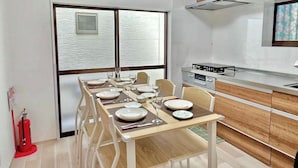 A modern kitchen with wooden cabinets, a gas stove, and a dining area set for six with white chairs and a large window offering a view.