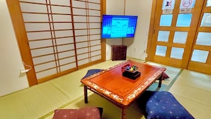 A traditional Japanese room with tatami flooring, a low wooden table, cushions, a television, and sliding doors.