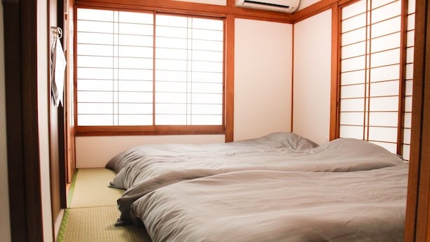 A traditional Japanese-style room with tatami flooring, sliding shoji doors, and a futon bed.