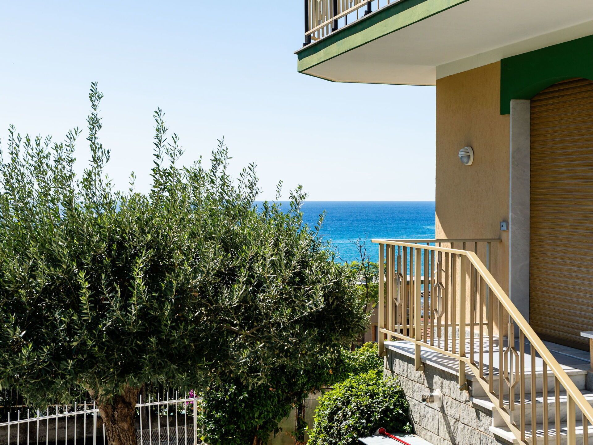 A balcony with a view of the sea, a tree, and a building facade.