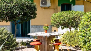 Un patio al aire libre con una mesa redonda y taburetes rojos, rodeado de plantas y árboles.
