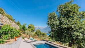 Uma piscina com espreguiçadeiras, cercada por vegetação e um muro de pedra.