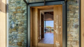 Interior moderno com parede de pedra, piso de madeira e porta de vidro que dá para área externa com vista das montanhas.