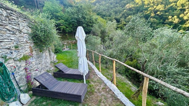 Eine Steinsäule, zwei Korbsessel, ein weißer Sonnenschirm und ein Garten mit Pflanzen und einem Kiesweg.