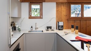 Una cuina moderna amb un vàter integrat, armaris de fusta, una cafetera i una finestra que mostra un paisatge nevós.
