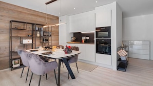 A modern kitchen with white cabinets, a built-in oven, and a dining area with a round table and chairs. - Beautiful apartment for 4 people with WIFI, TV, terrace and panoramic view (Crans-montana)