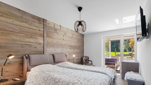 A bedroom with a large bed, a wooden accent wall, a desk with a lamp, and a view of the outdoors. - Beautiful apartment for 4 people with WIFI, TV, terrace and panoramic view (Crans-montana)