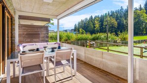 A covered outdoor seating area with a table and chairs, a wooden deck, and a view of a forested landscape. - Beautiful apartment for 4 people with WIFI, TV, terrace and panoramic view (Crans-montana)