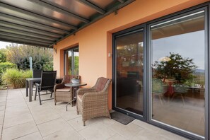 A covered patio area with a table and chairs, a sliding glass door leading to an indoor space, and a view of the outdoors. - Holiday Apartment Bär, 59 sqm, 1 Bedroom, Living and Dining Area, max. 3 Persons (Rosengarten)