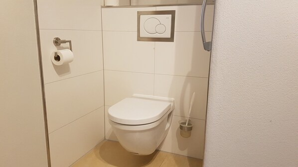Un baño pequeño y blanco con inodoro, dispensador de toallas de papel y palanca de descarga.
