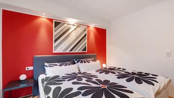 Een slaapkamer met een bed, nachtkastje, wandlamp en een rode accentmuur.