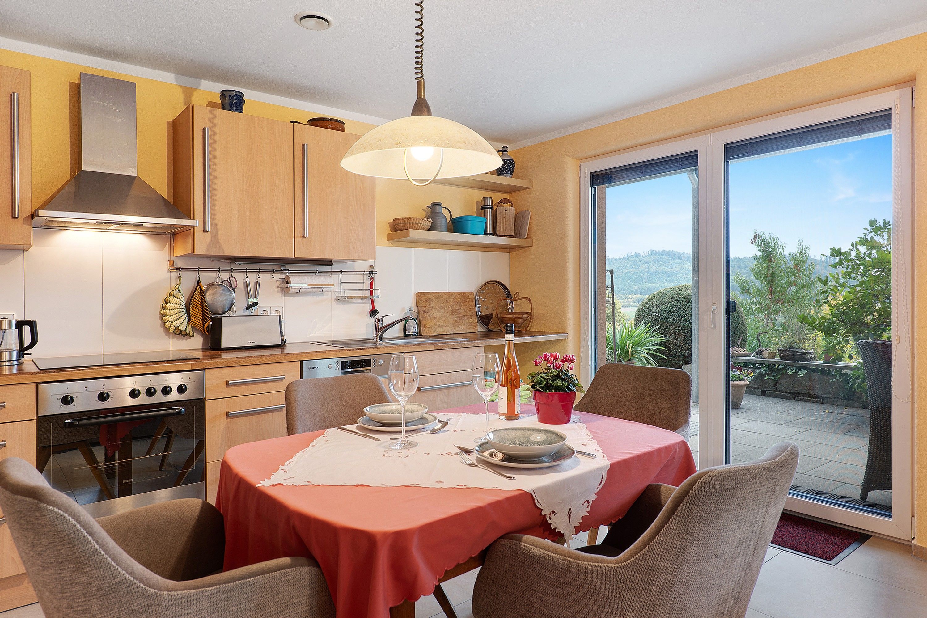 A modern kitchen with a dining area, large windows, and a view of the outdoors.
