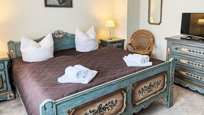 Un dormitorio con una cama grande, una silla, un tocador, una lámpara y un cuadro en la pared.