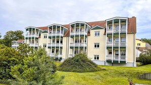 Un hotel de varios pisos con balcones, un césped verde y un pequeño jardín.