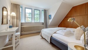 Ett sovrum med en säng, ett nattduksbord, en lampa, ett element och ett fönster med gardiner.