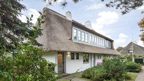 Ett traditionellt hus med ett halmtak, en ytterdörr och en liten trädgård.