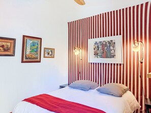 A bed with pillows, a red and white striped wall, and framed artwork.