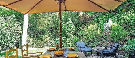 An outdoor patio with a wooden table, yellow chairs, a blue chair, and a large umbrella.