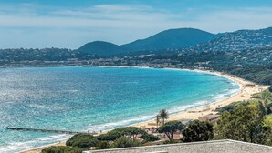 Une vue côtière avec une plage, une eau d’un bleu limpide et une chaîne de montagnes en arrière-plan.