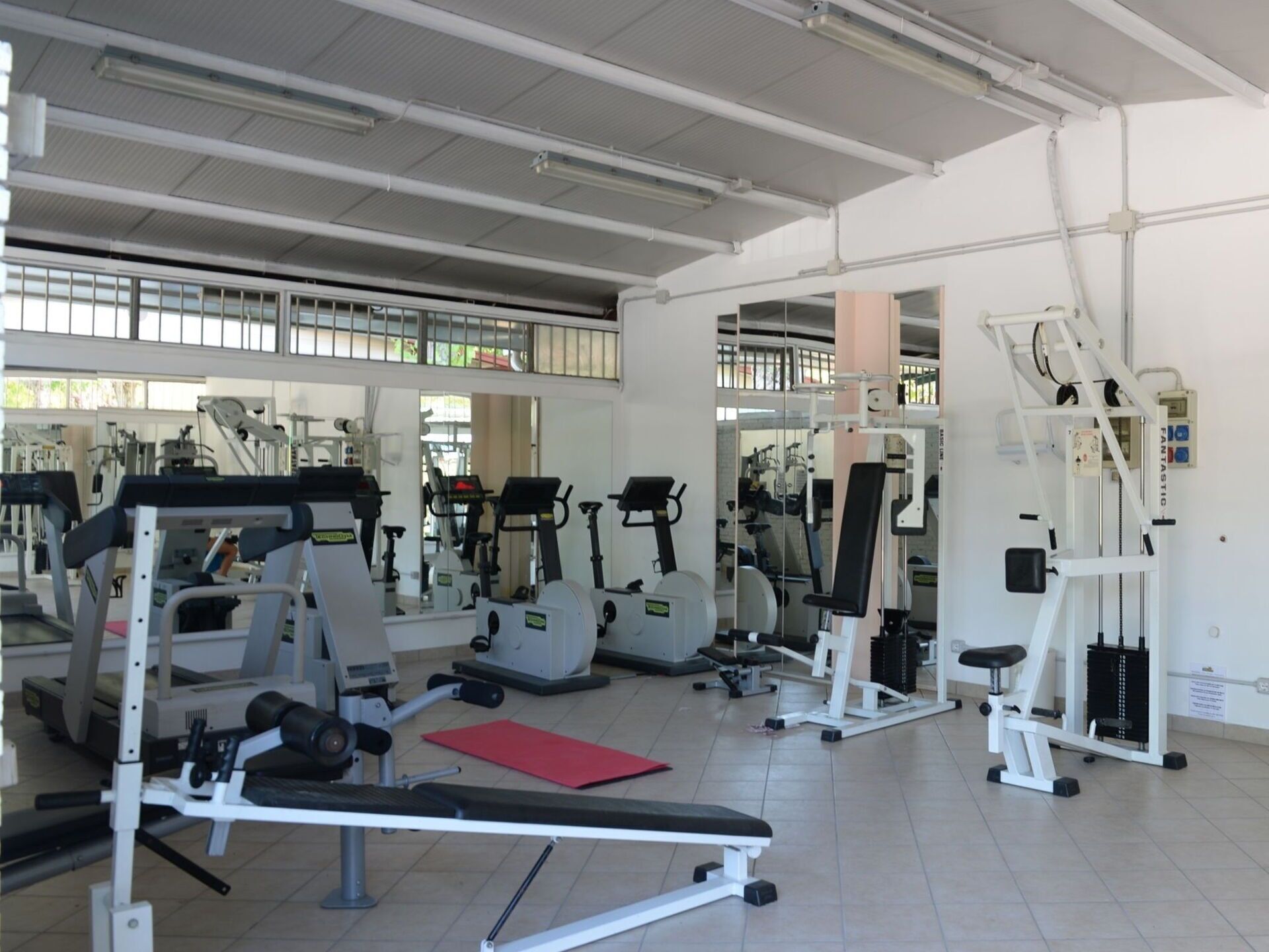 A gym with various exercise machines, a red mat, and a bench.