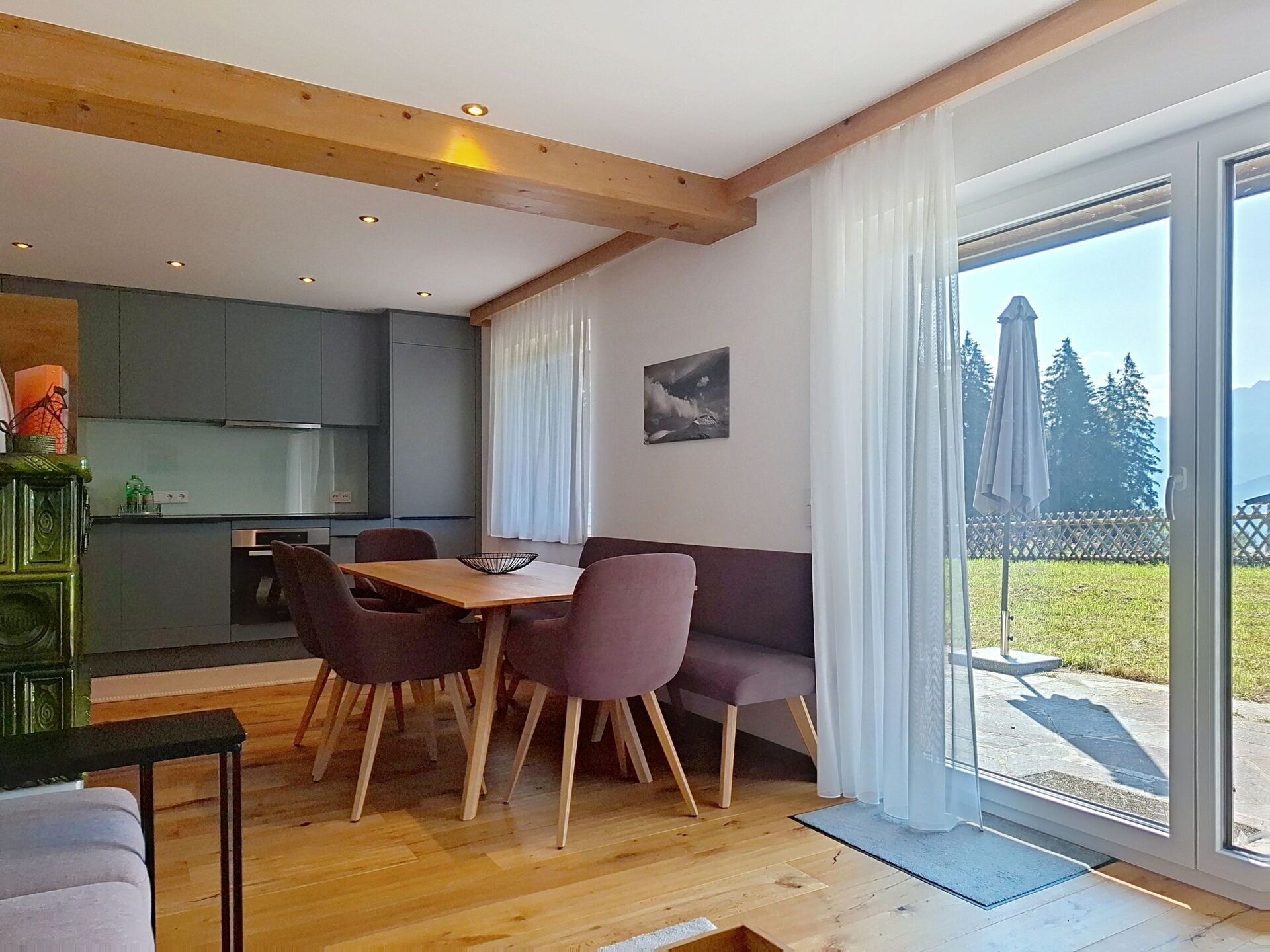A modern kitchen with wooden beams, a dining area with a table and chairs, and a large sliding glass door leading to a deck.