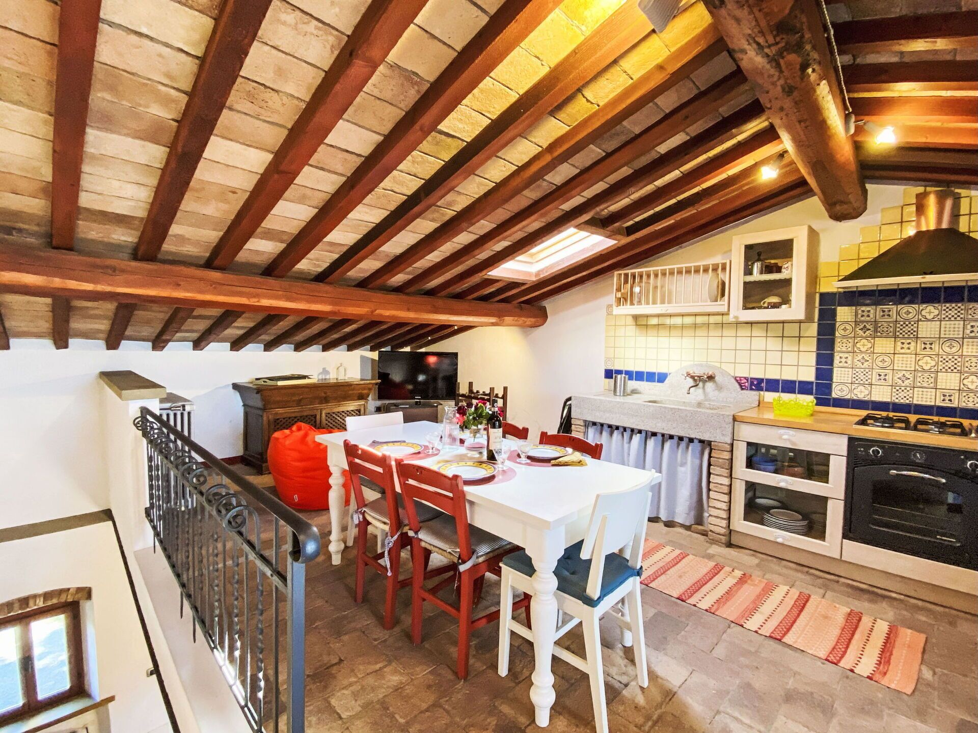 Una cocina rústica con comedor, vigas de madera, salpicadero de azulejos y suelo de piedra.