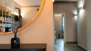 A modern interior with a curved wooden bench, a wall-mounted mirror, and a pendant light. A hallway extends into the distance with a door at the end.