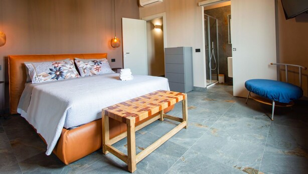 A bedroom with a bed, bedside table, bench, and a shower area.