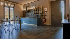 A modern kitchen with a central island, blue cabinetry, and a built-in stove. There is a fire extinguisher mounted on the wall and a window with blinds.