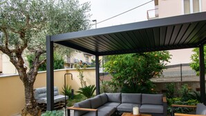 An outdoor patio with a covered seating area, stone flooring, and potted plants.