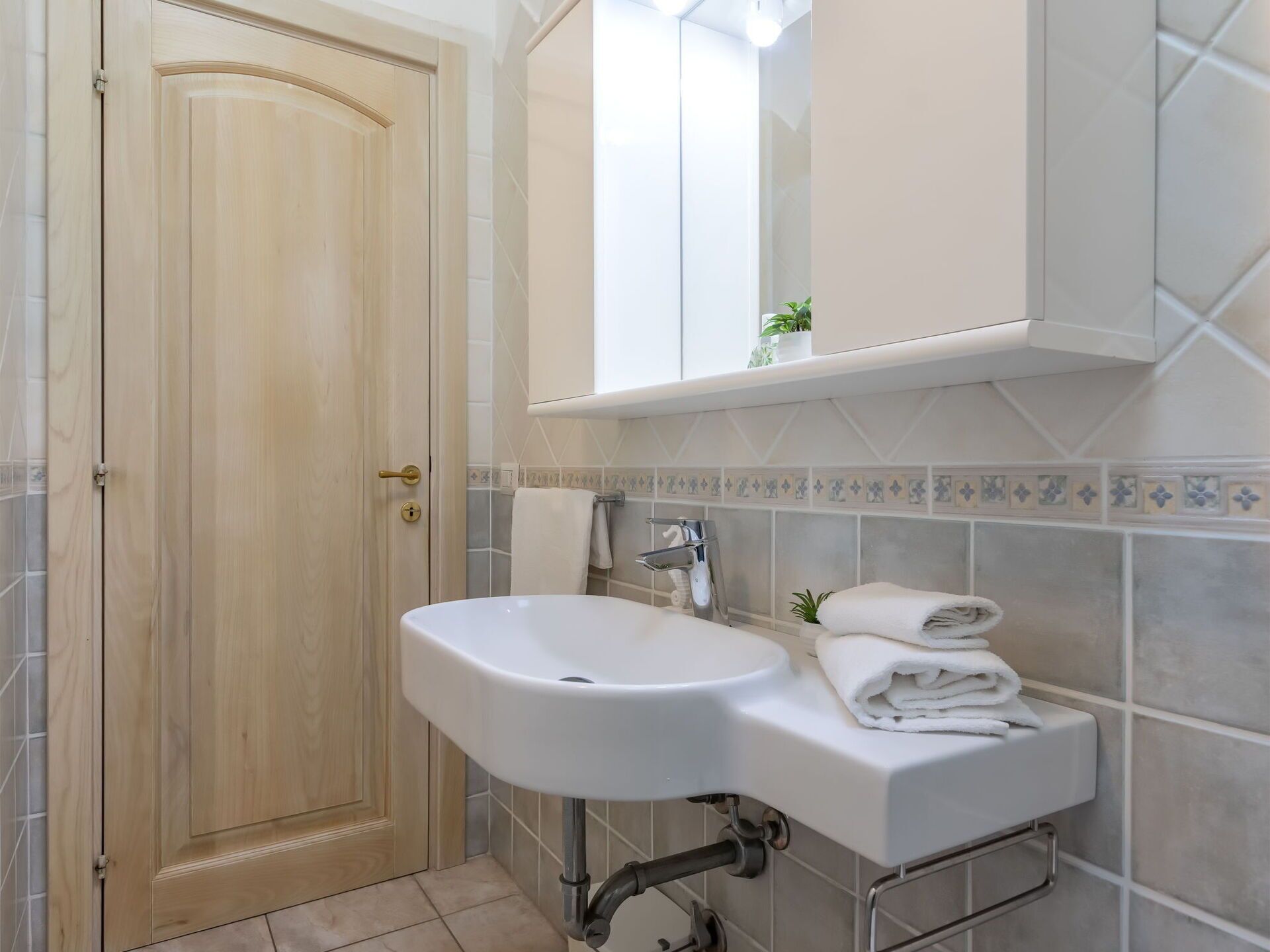 Un baño con puerta de madera, lavamanos blanco, toallero y espejo sobre el lavamanos.