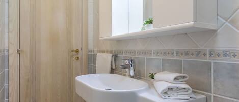 Un baño con puerta de madera, lavamanos blanco, toallero y espejo sobre el lavamanos.