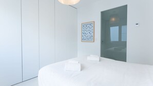 A modern hotel room with a large bed, a wardrobe, a framed artwork, and a door.