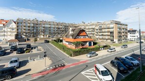 A residential area with multi-story apartment buildings, a central roundabout, and a small traditional house with a thatched roof.