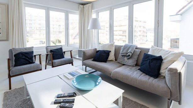 A modern living room with a sofa, two armchairs, a coffee table, and a large window offering a view of buildings.
